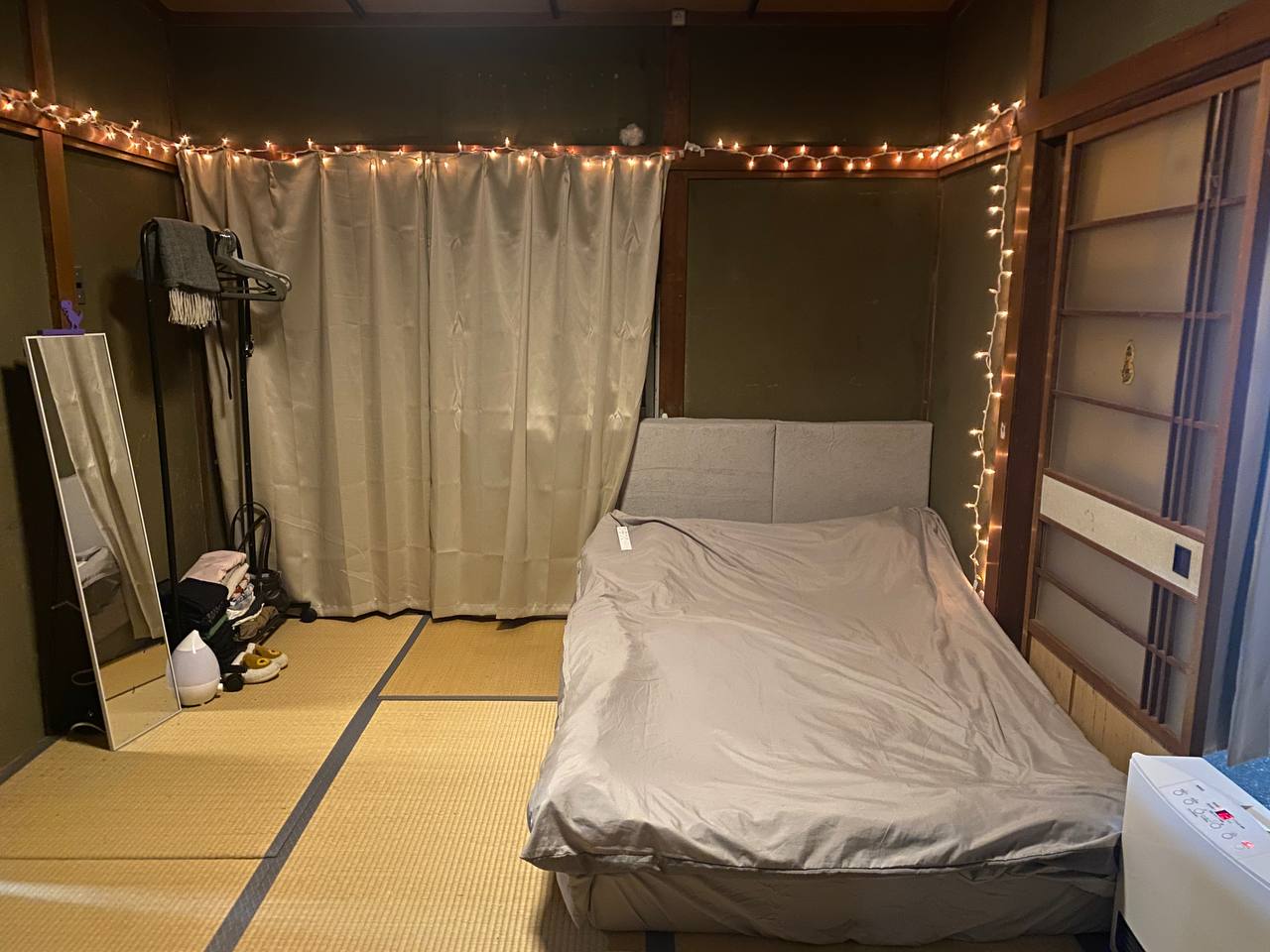 A tatami sleeping room at the Kaizen Dojo, low bed made up against a curtained wall, timber frame and string lights above.