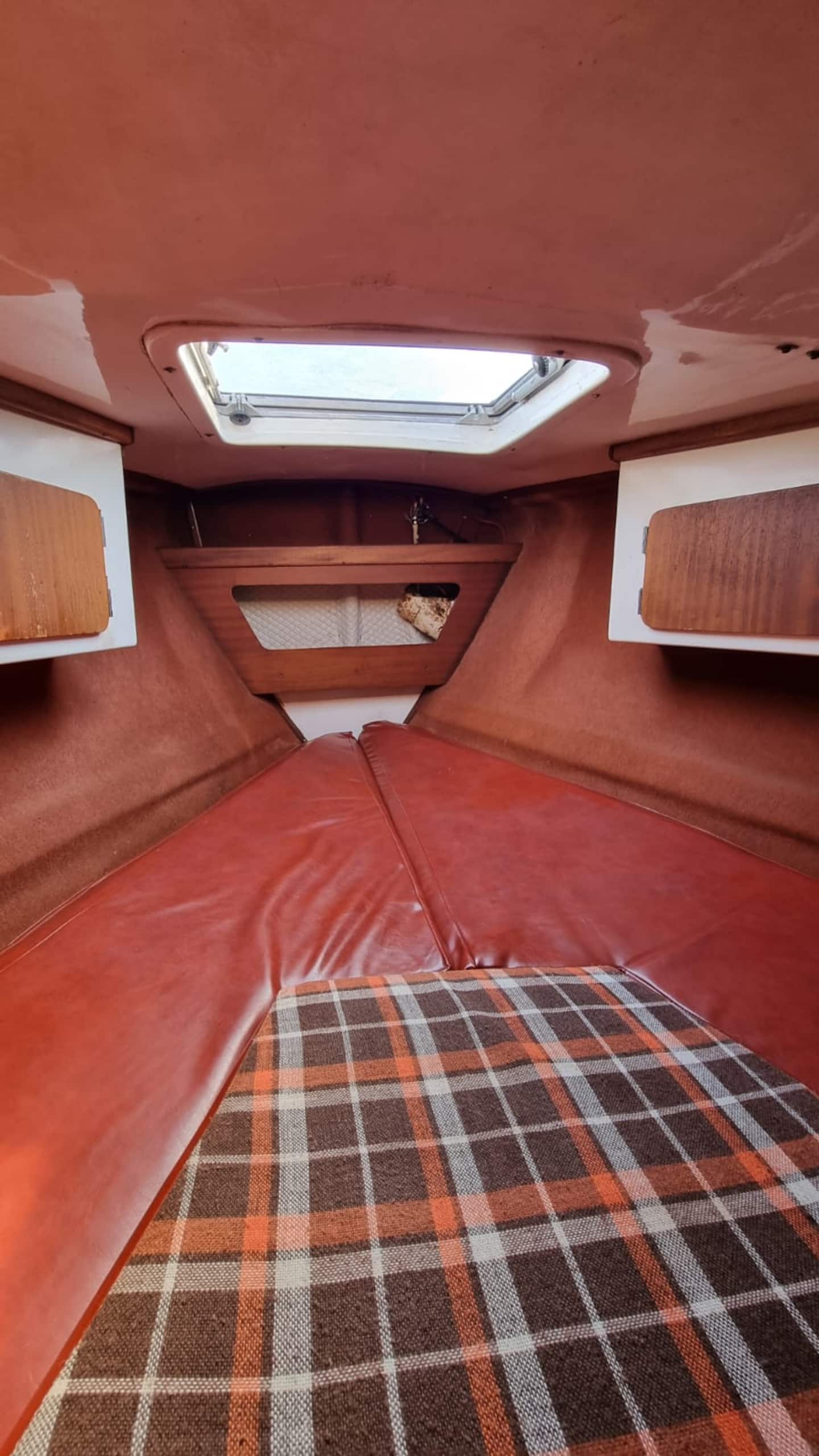 The forward V-berth cabin of the Monaco sailboat, a double bunk in red upholstery set into the bow with lockers above.