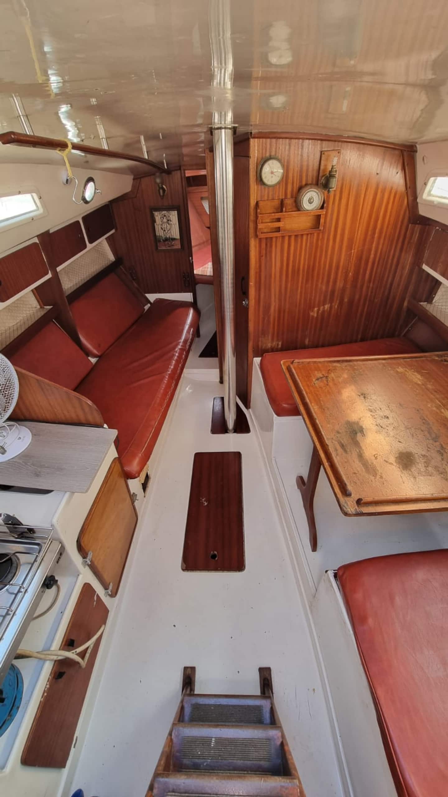 The saloon table of the Monaco sailboat folded out between the red bench seats, with the timber sole and companionway behind.