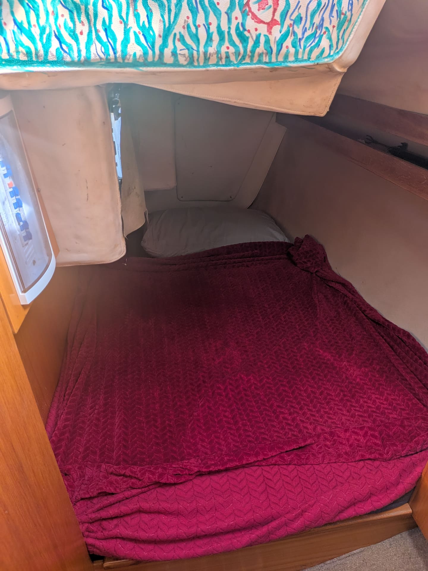 The forward cabin of the Varazze sailboat, a double berth made up with a deep red cover, tucked under the curve of the hull.